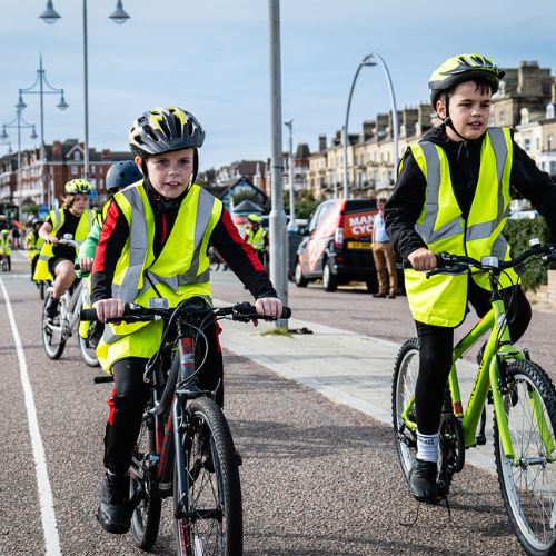 A picture of two children in high visibility clothing cycling on their bike on a cycling path.